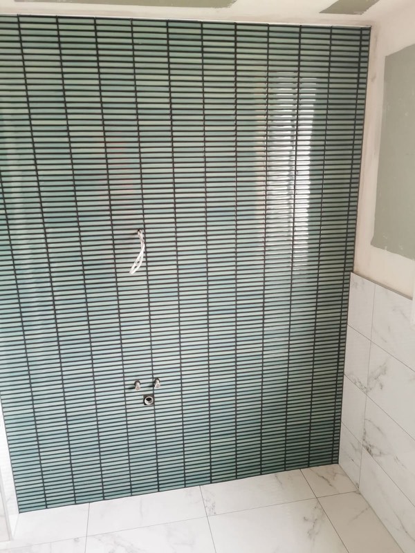 Green stacked mosaic feature wall above a marble-look tiled floor